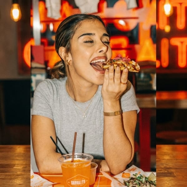 A woman with closed eyes happily bites into a taco at a restaurant with neon signs.