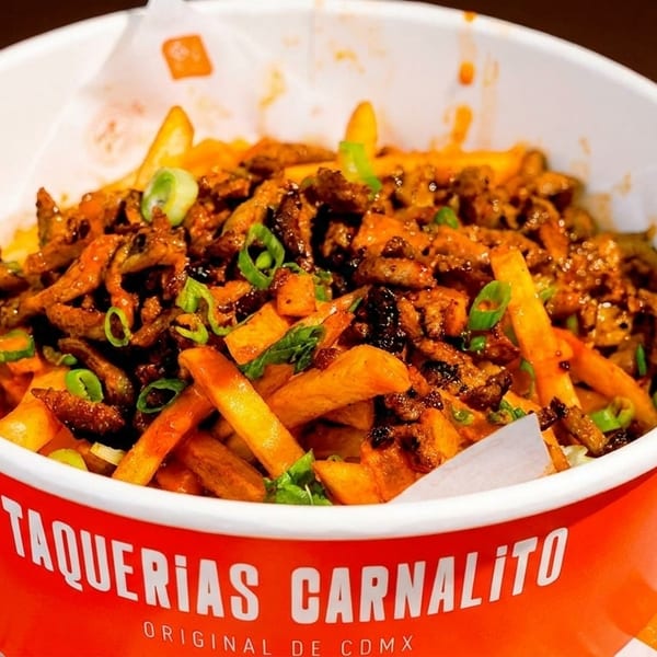 Taquerias Carnalito's loaded fries with meat and green onions in an orange and white cup.