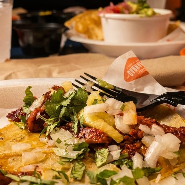 Close-up of a delicious al pastor taco with pineapple, onions, and cilantro on a white plate.