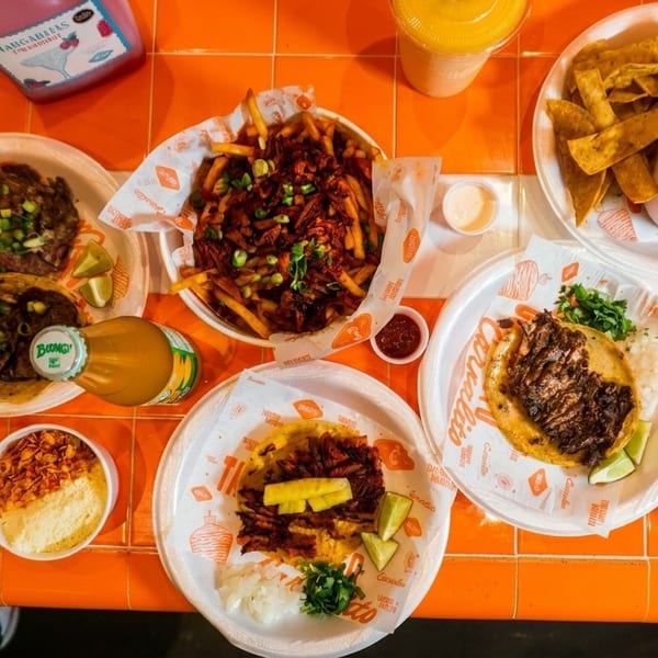Overhead view of a vibrant orange table laden with various Mexican dishes and drinks.